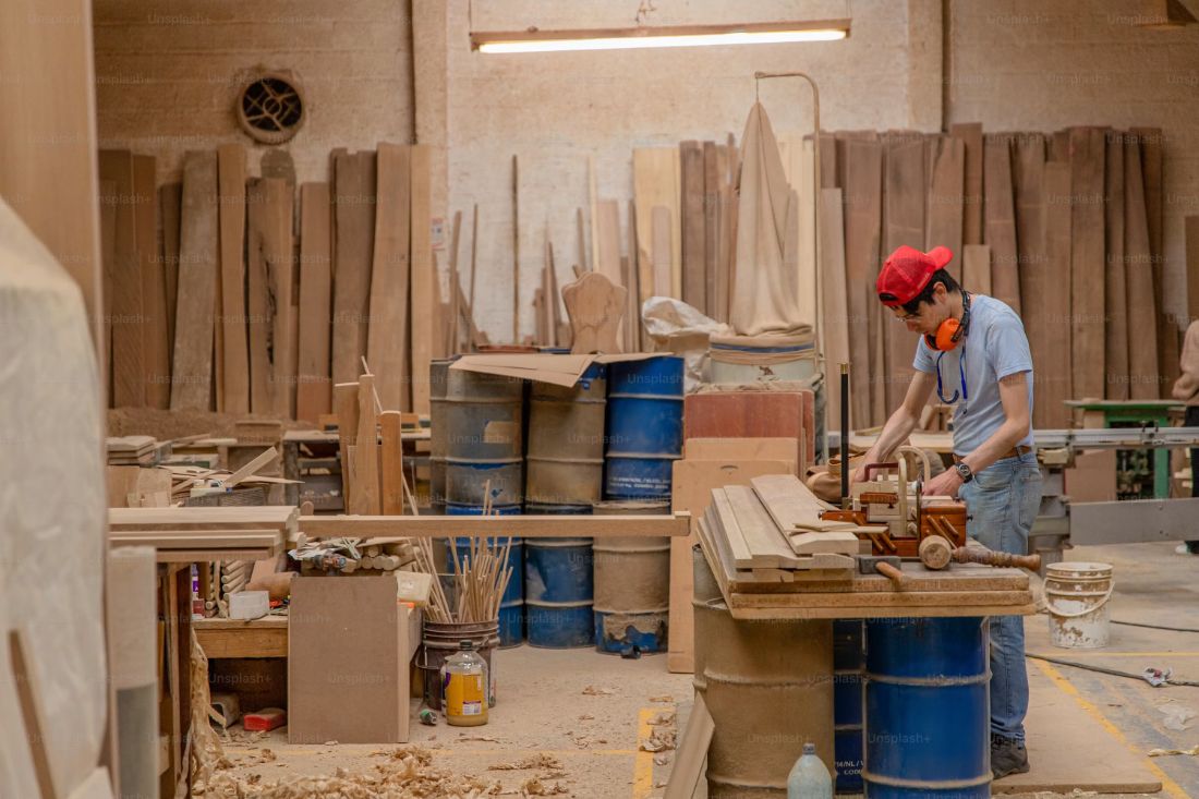 Carpintero trabajando una tabla en su taller de CABA rodeado de tablones y maquinaria, donde se fabrican las bases y paneles de reemplazo para muebles de cocina dañados por humedad
